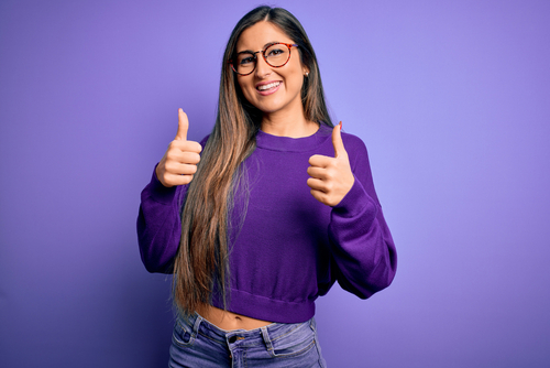 woman in violet shirt holding both her thumbs up