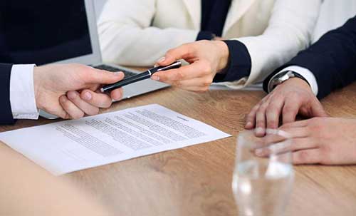 a person handing a black pen to another to sign a document