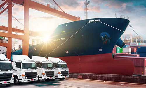 four white trucks and a large cargo ship at the background