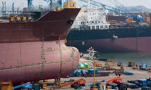 one cargo ship on water while another receiving maintenance