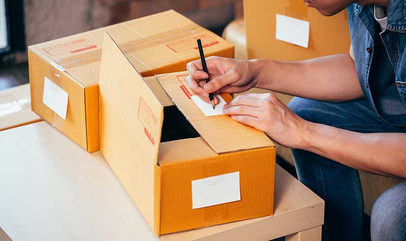 person writing a note on a partially opened cardboard box