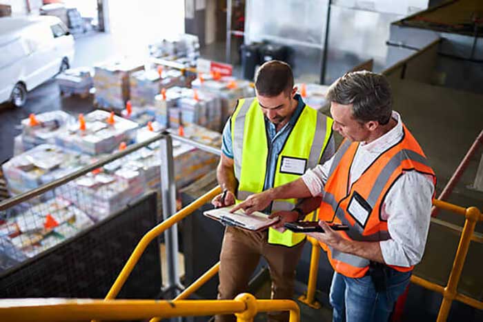 two men wearing reflective vests looking at some paperwork