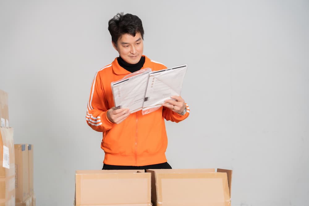 man in orange sweater ckecking paperwork with two open boxes in front