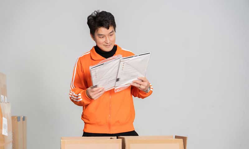 man standing behind two open cardboard boxes checking paperwork