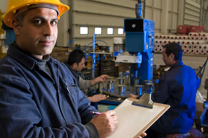 man wearing safety gear holding a clipboard with 2 guys at the background