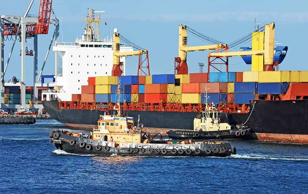 large cargo ship being taxied out of the port by two tugboats