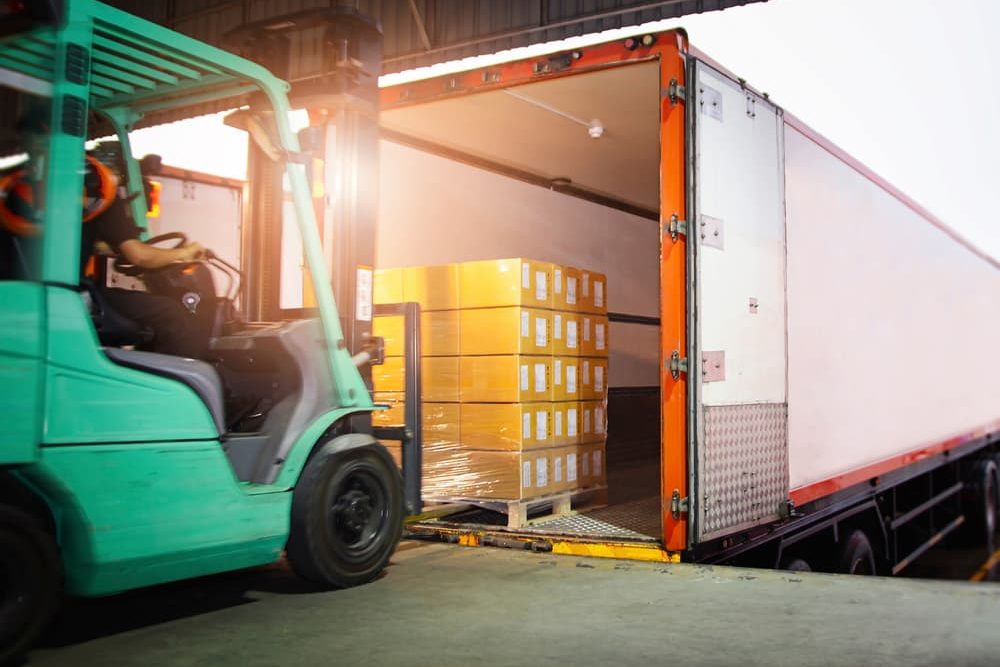green forklift loading packages in a trailer